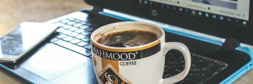 A laptop, cellphone and a coffee mug as an author prepares to write essays using ChatGPT.