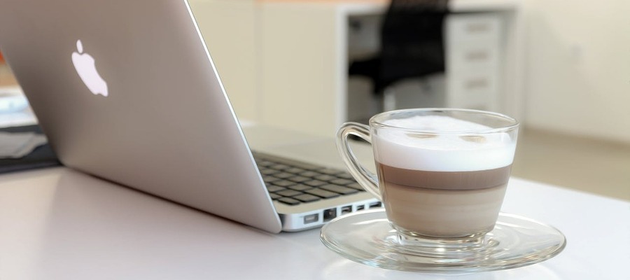 A Mac laptop next to a cup of coffee.