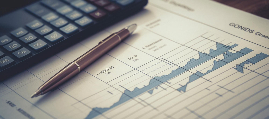 A financial calculator and a pen on top of the financial report with graphs.