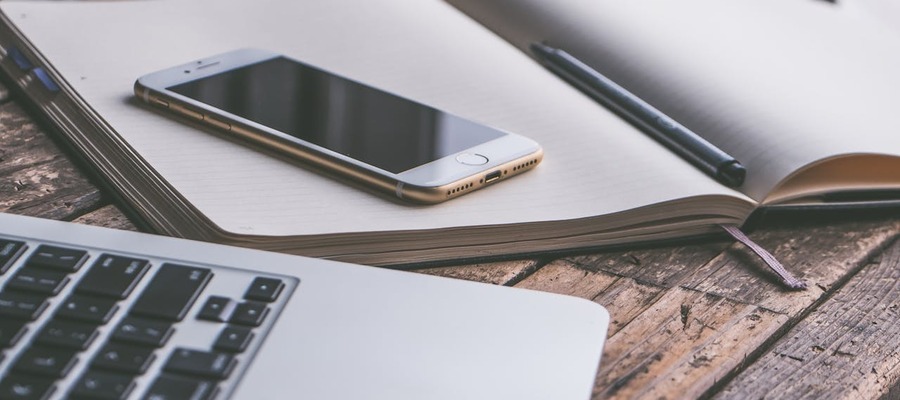 A laptop, smart phone, book and pen used for studying for certification for artificial intelligence.